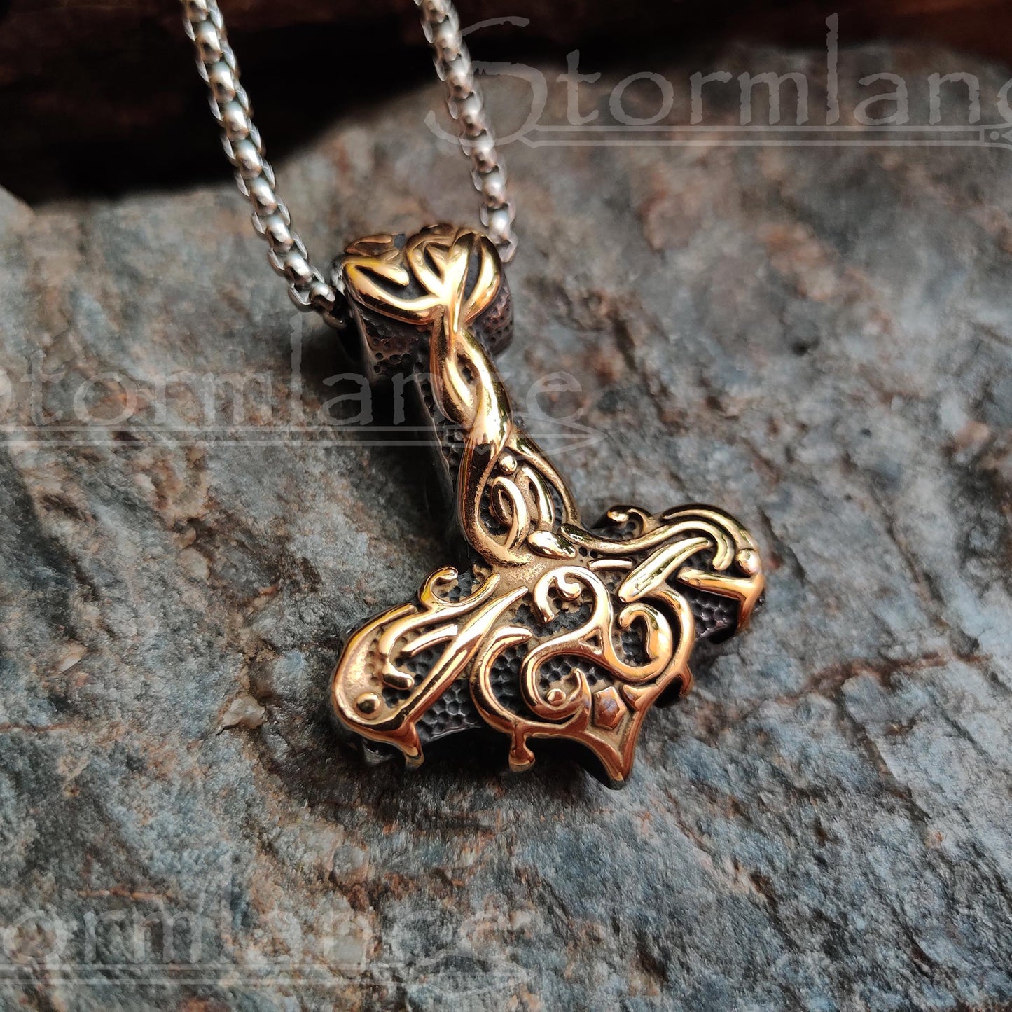 Mjolnir pendant with golden scandinavian pattern made of stainless steel, laying on a granite stone slab