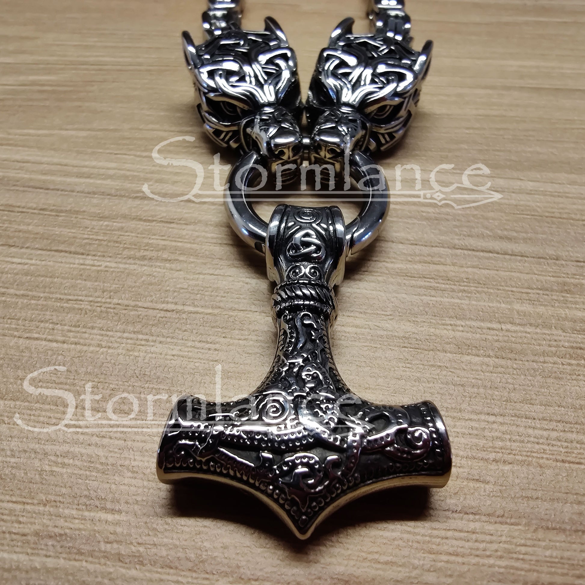 massive thor's hammer pendant with geri and freki wolves, made of stainless steel, laying on a wooden desk