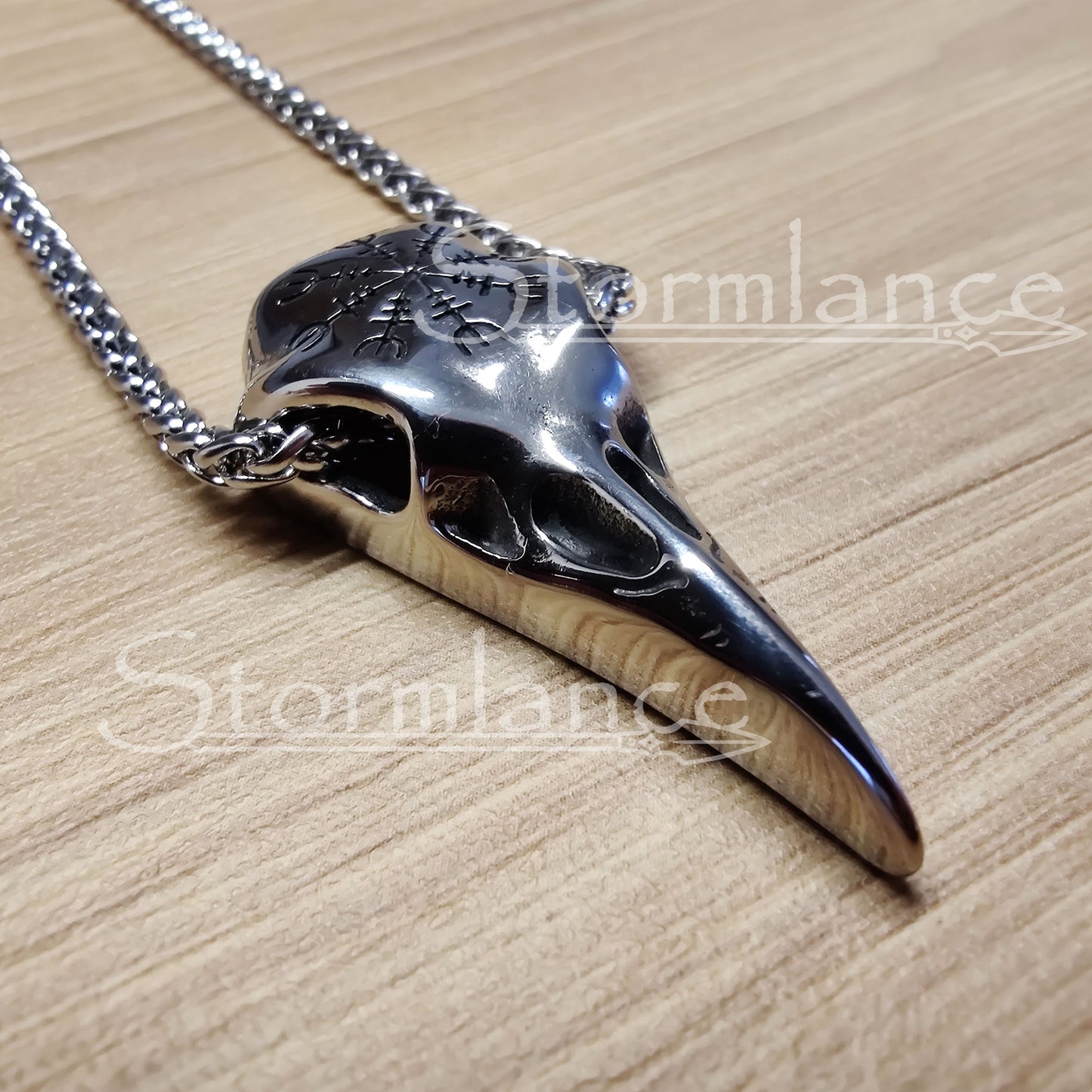 raven skull pendant with helm of awe made of stainless steel, laying on a wooden desk