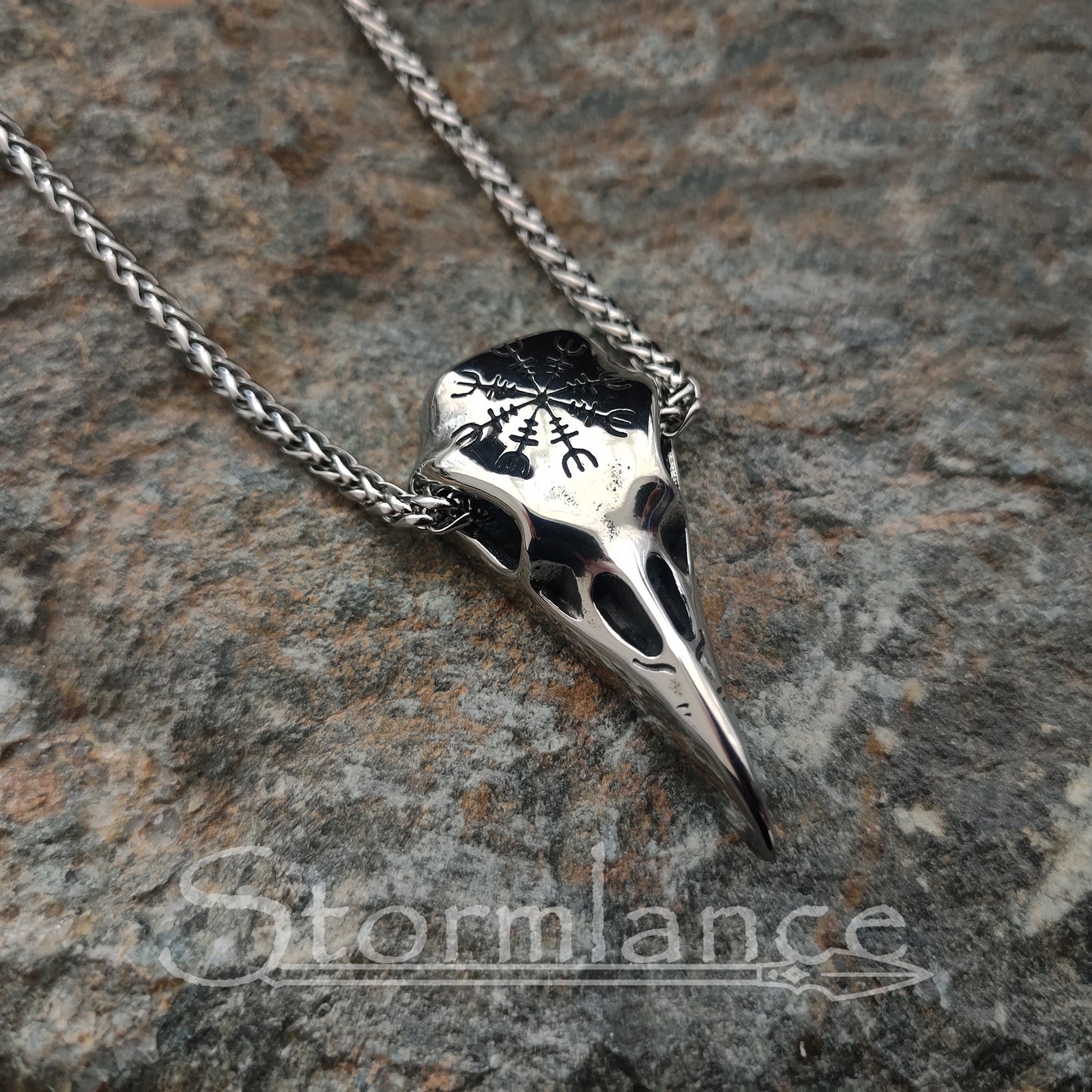 raven skull pendant with helm of awe made of stainless steel, laying on a granite stone slab