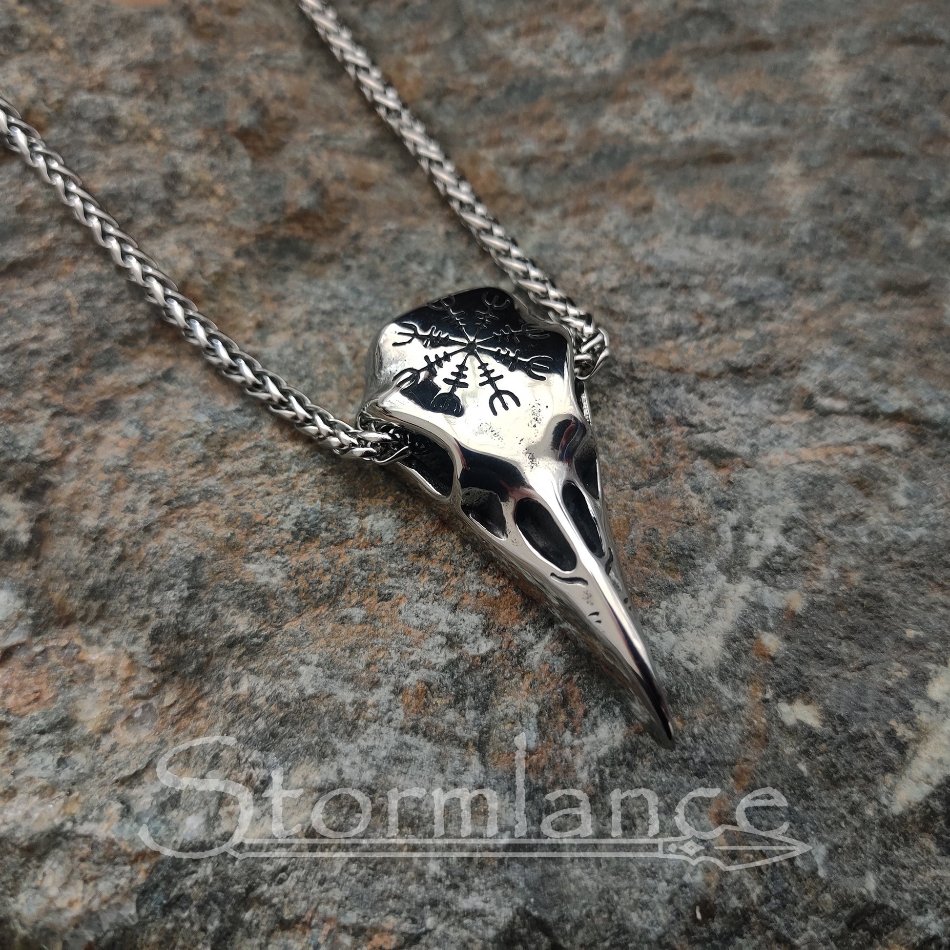 raven skull pendant with helm of awe made of stainless steel, laying on a granite stone slab