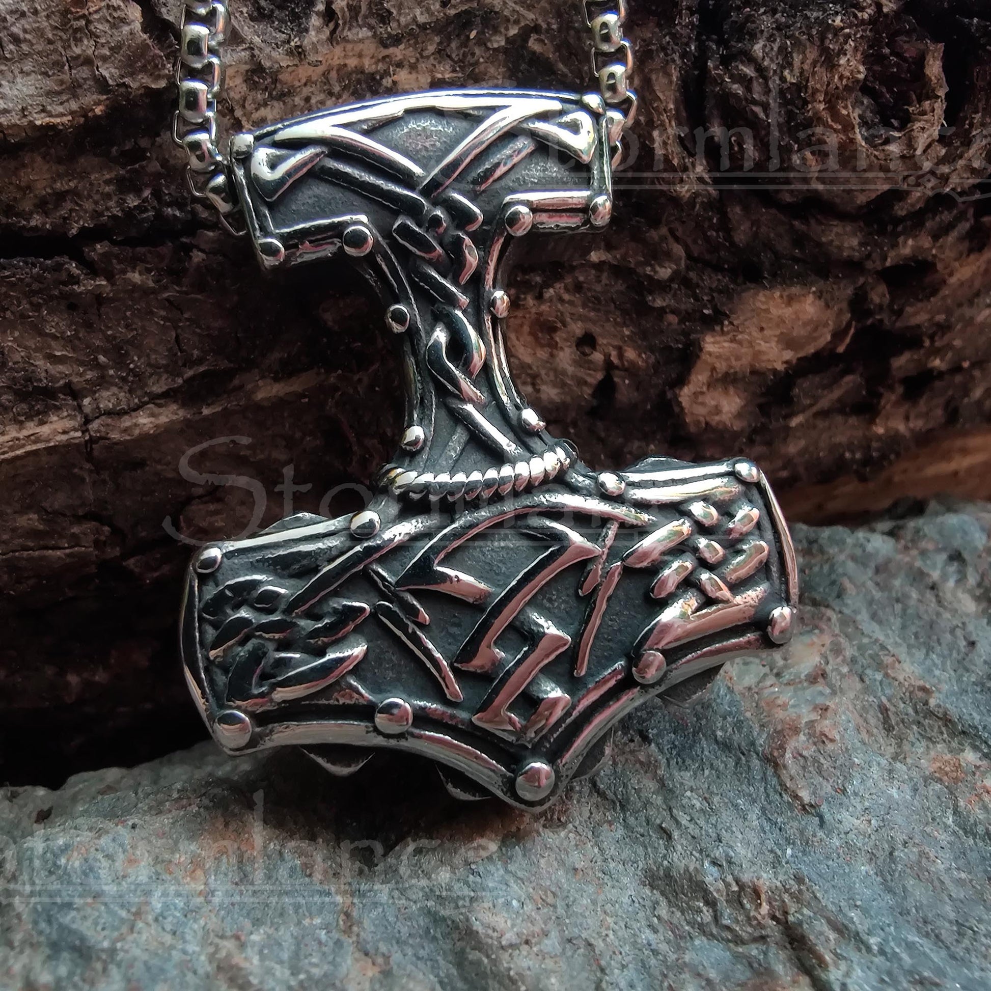 Massive mjolnir pendant with scandinavian pattern  made of stainless steel, laying on a granite stone slab