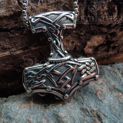 Massive mjolnir pendant with scandinavian pattern  made of stainless steel, laying on a granite stone slab
