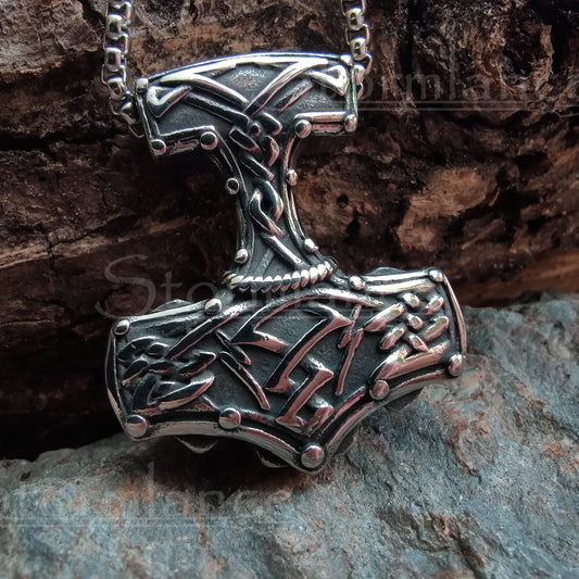 Massive mjolnir pendant with scandinavian pattern  made of stainless steel, laying on a granite stone slab