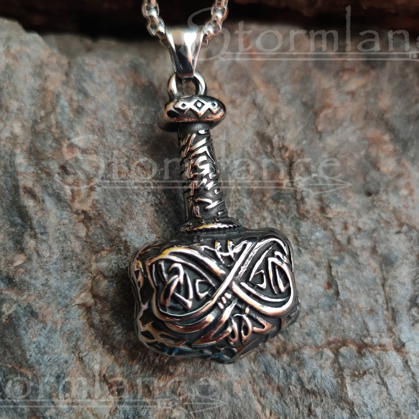 Heavy mjolnir pendant with scandinavian pattern made of stainless steel, laying on a granite stone slab