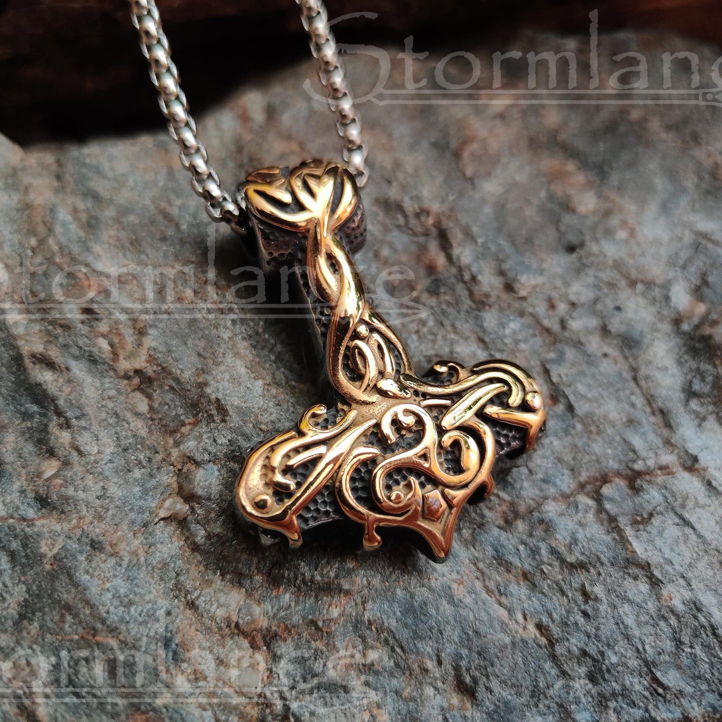 Mjolnir pendant with golden scandinavian pattern  made of stainless steel, laying on a granite stone slab