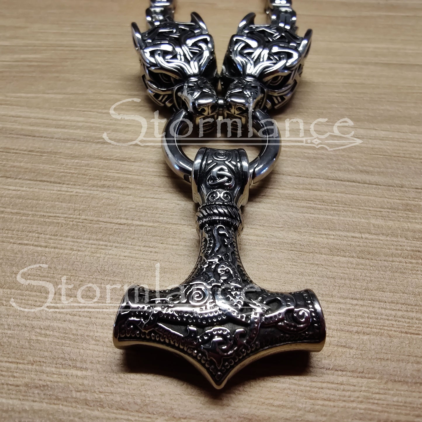 massive thor's hammer pendant with geri and freki wolves, made of stainless steel, laying on a wooden desk