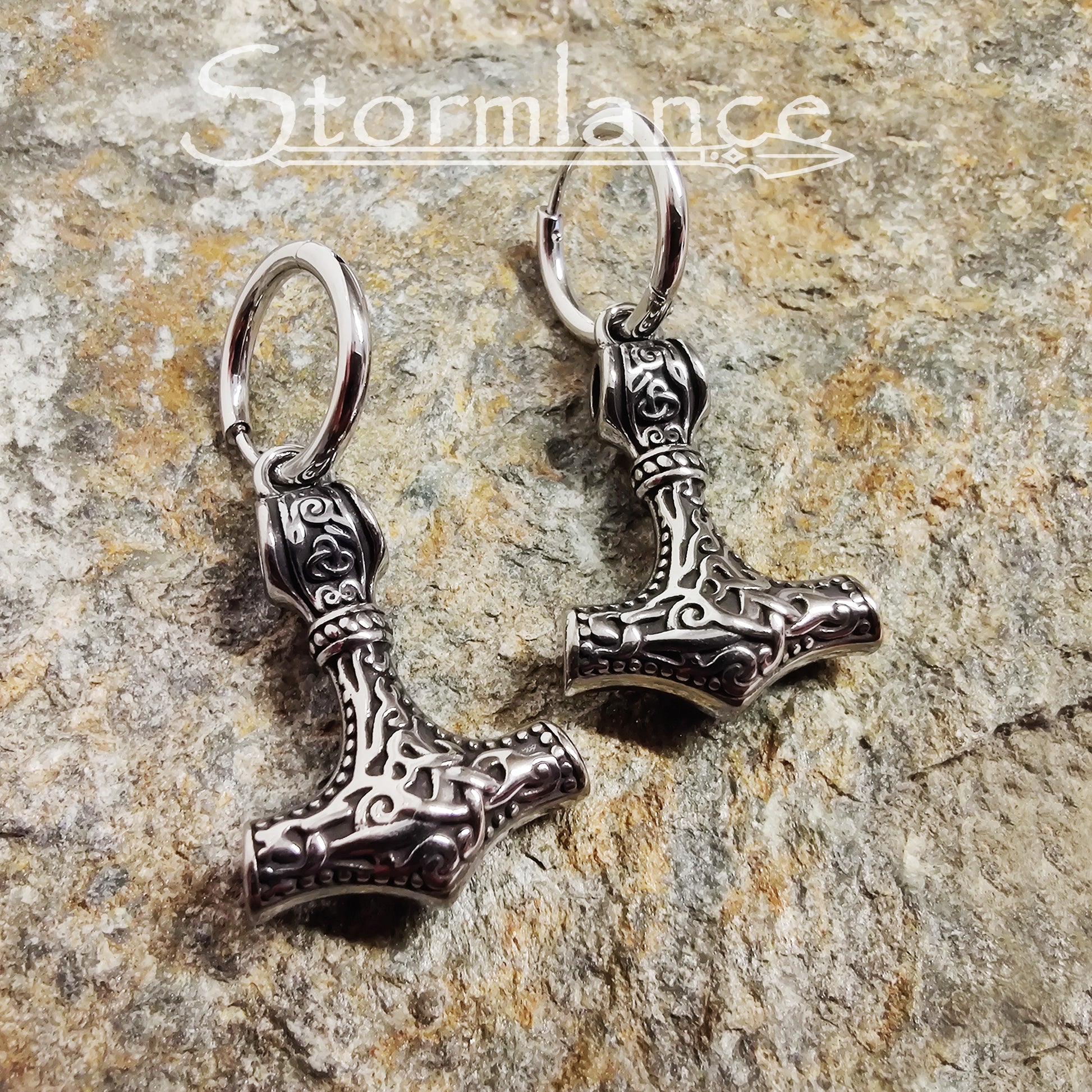 Mjolnir Earrings Silver in Color made of stainless steel laying on a stone slab