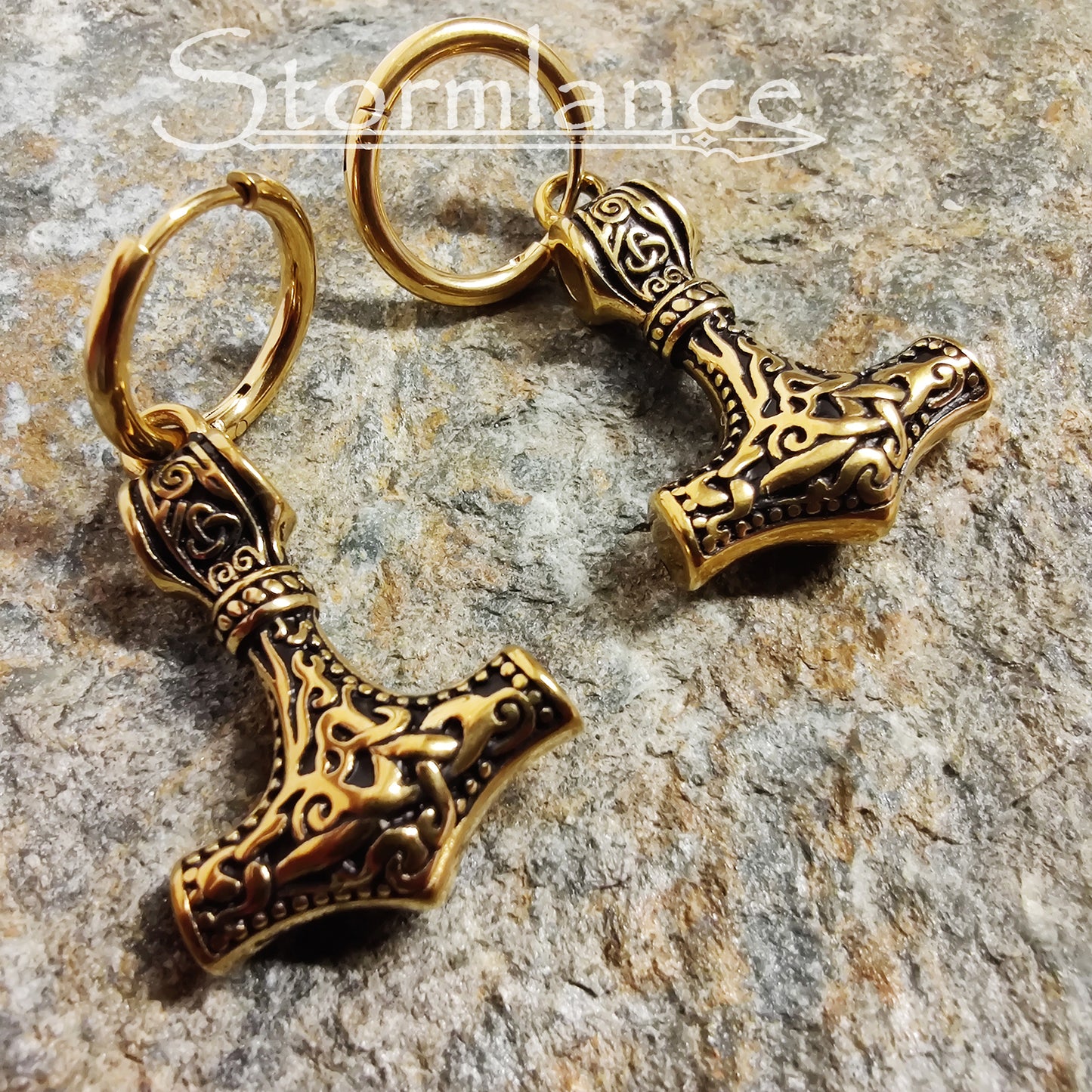 Mjolnir Earrings Gold in Color made of stainless steel laying on a stone slab