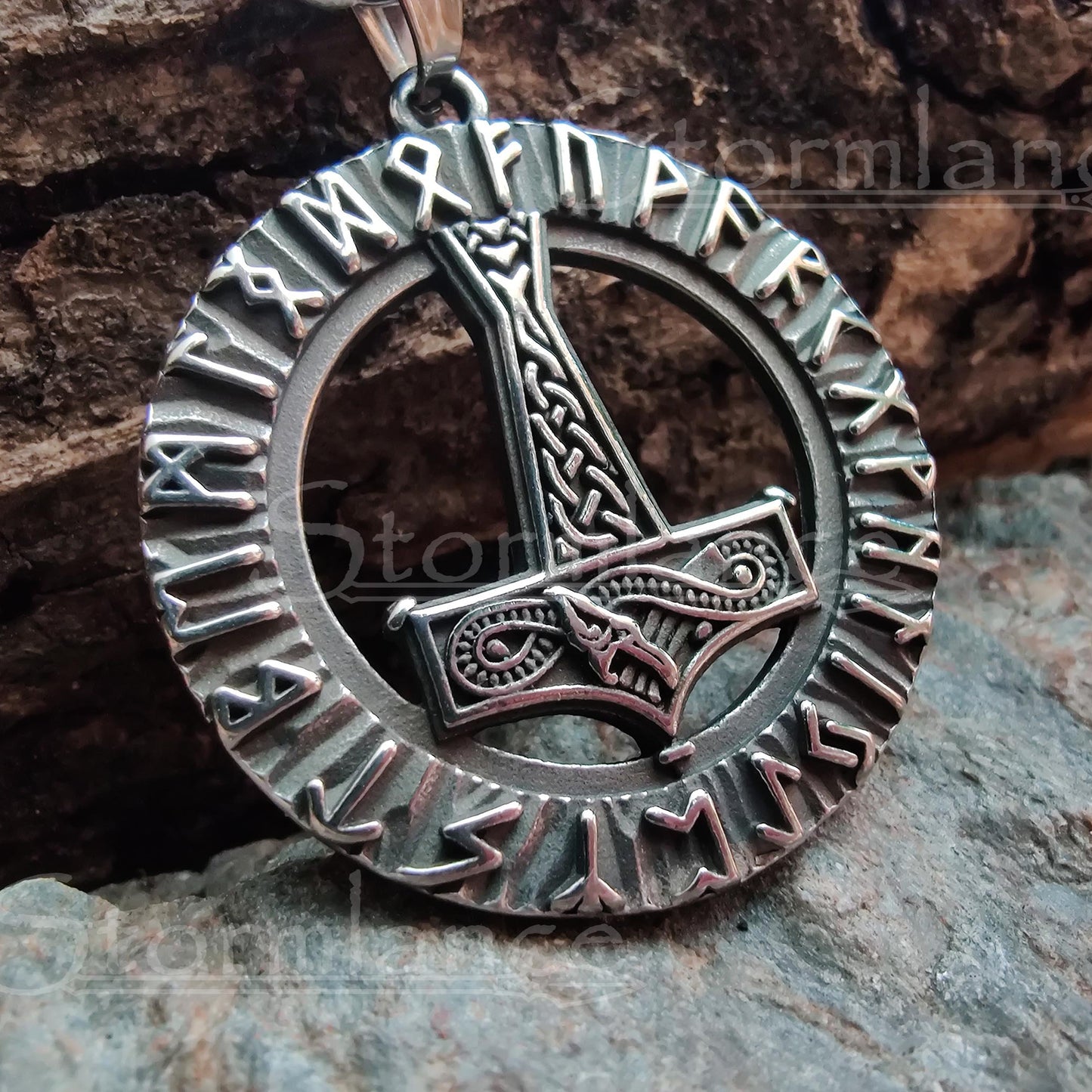 Mjolnir with elder futhark runes pendant made of stainless steel, laying on a granite stone slab