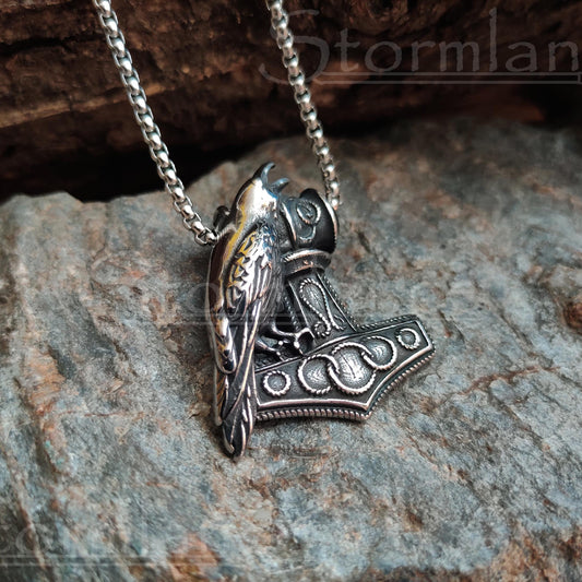 Mjolnir with raven pendant made of stainless steel, laying on a granite stone slab