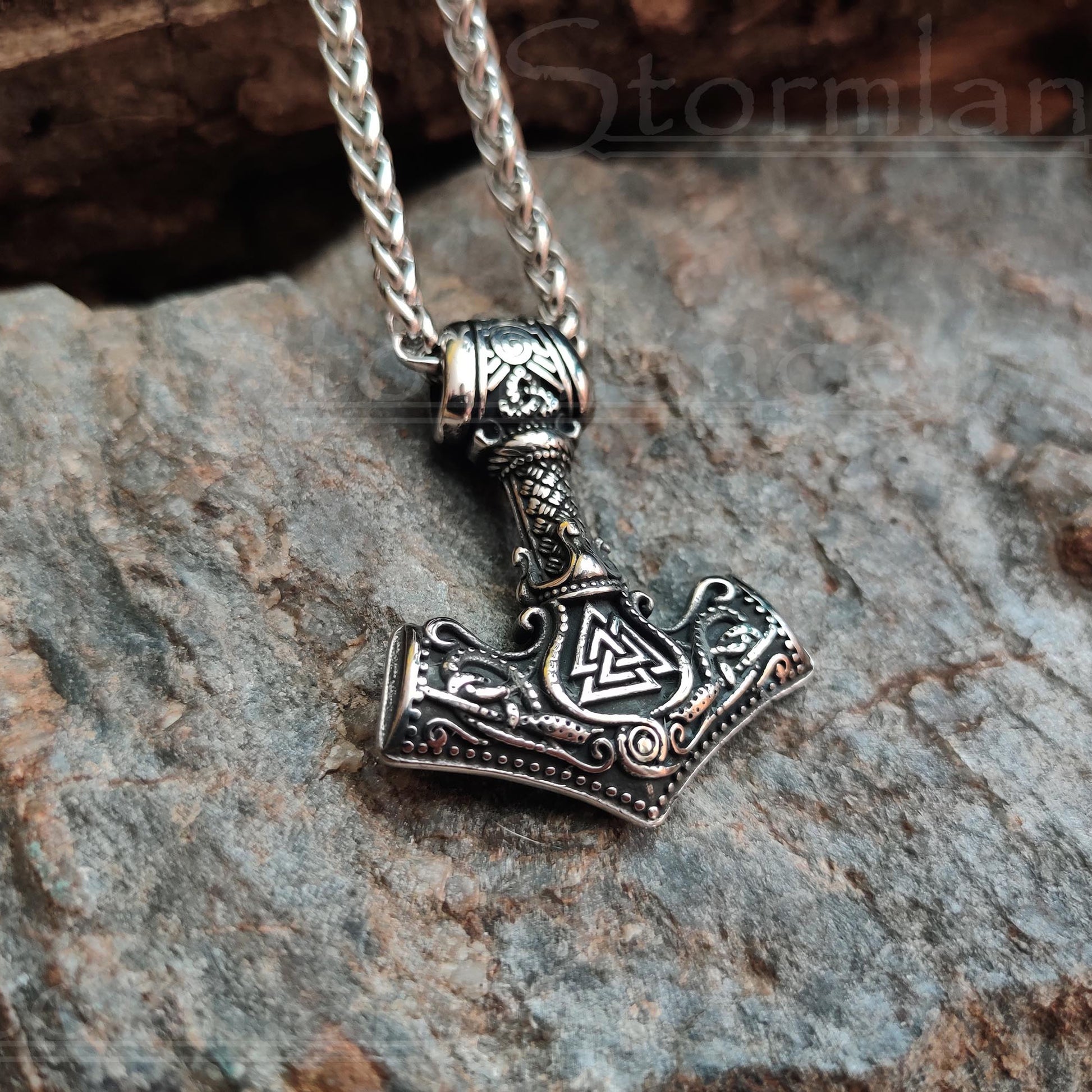 Mjolnir pendant with valknut and tiwaz rune made of stainless steel, laying on a granite stone slab