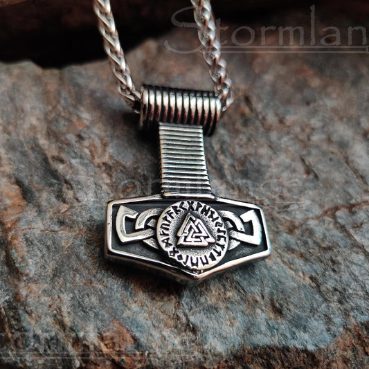 thor's hammer pendant with elder futhark runes and valknut made of stainless steel, laying on a granite stone slab