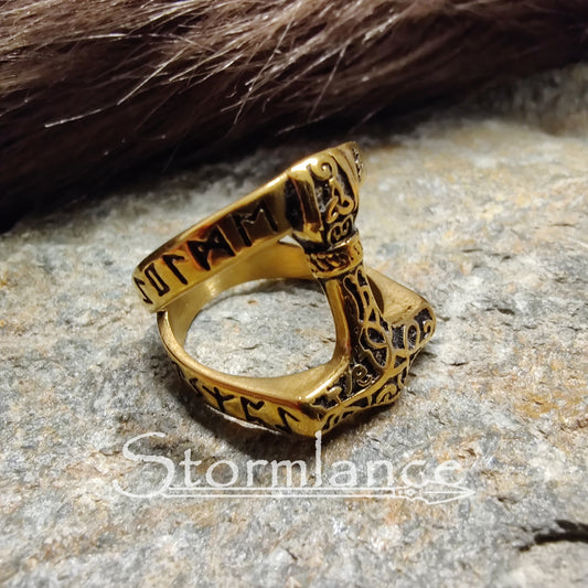 thor's hammer ring in gold color made of stainless steel, laying on a granite stone slab