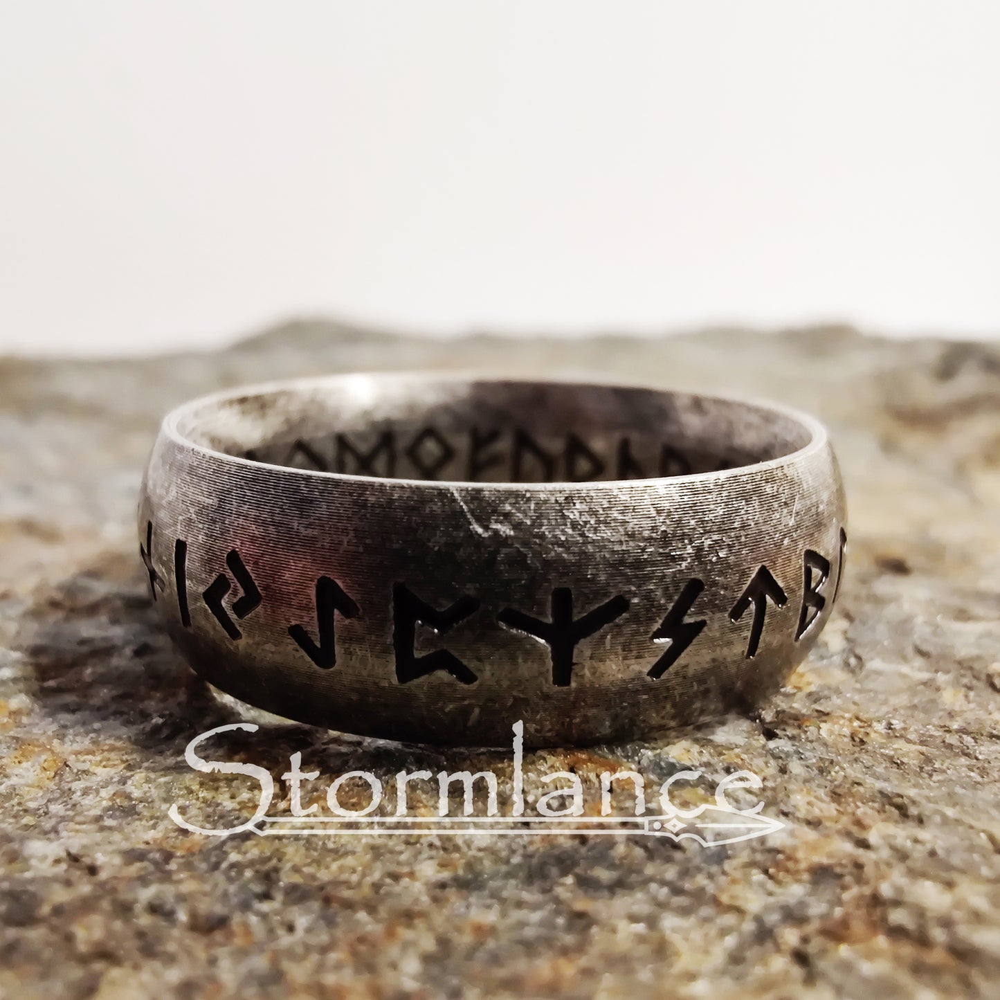 elder futhark runes ring made of stainless steel, laying on a granite stone slab