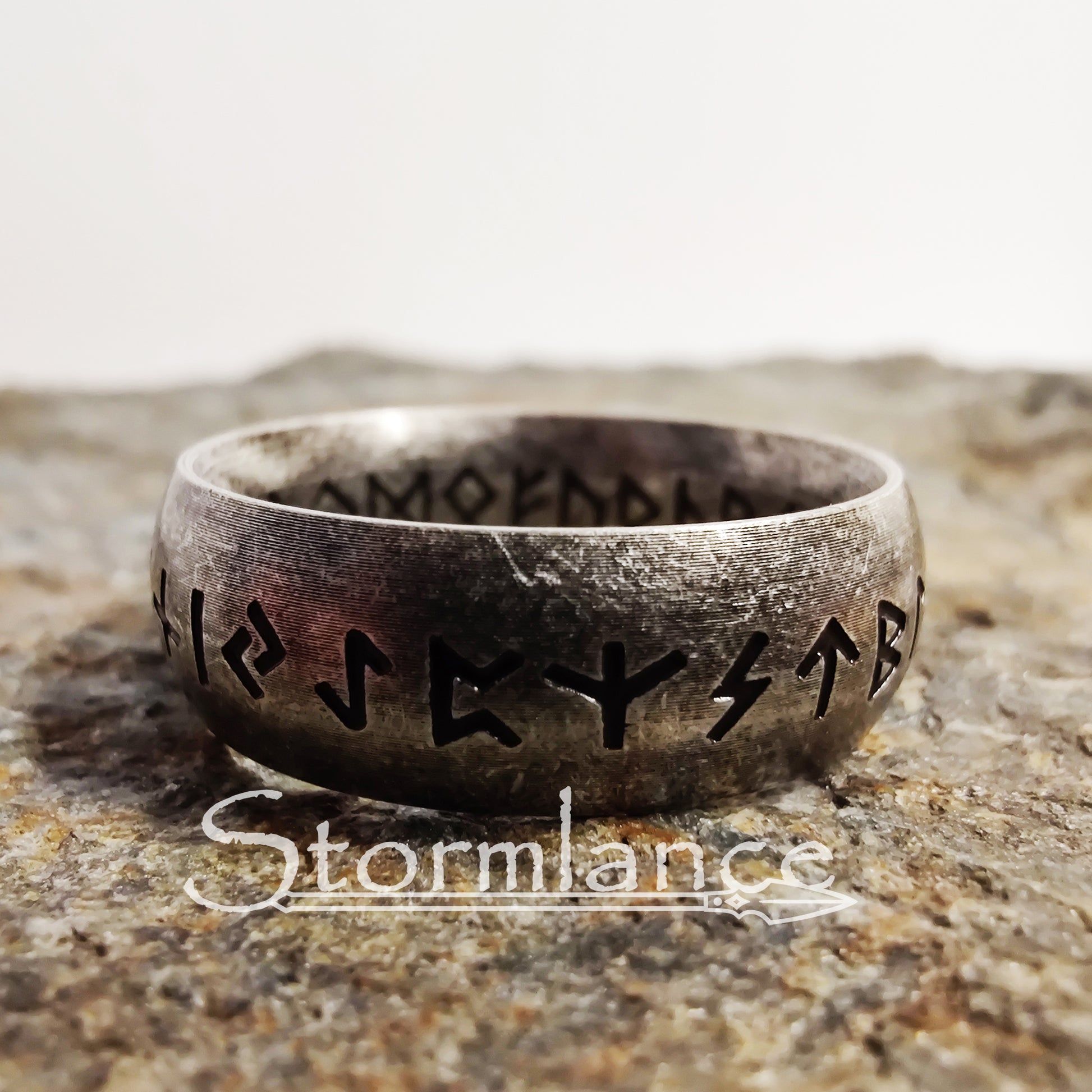elder futhark runes ring made of stainless steel, laying on a granite stone slab