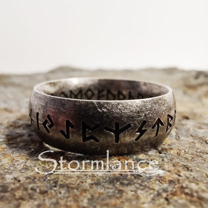 elder futhark runes ring made of stainless steel, laying on a granite stone slab