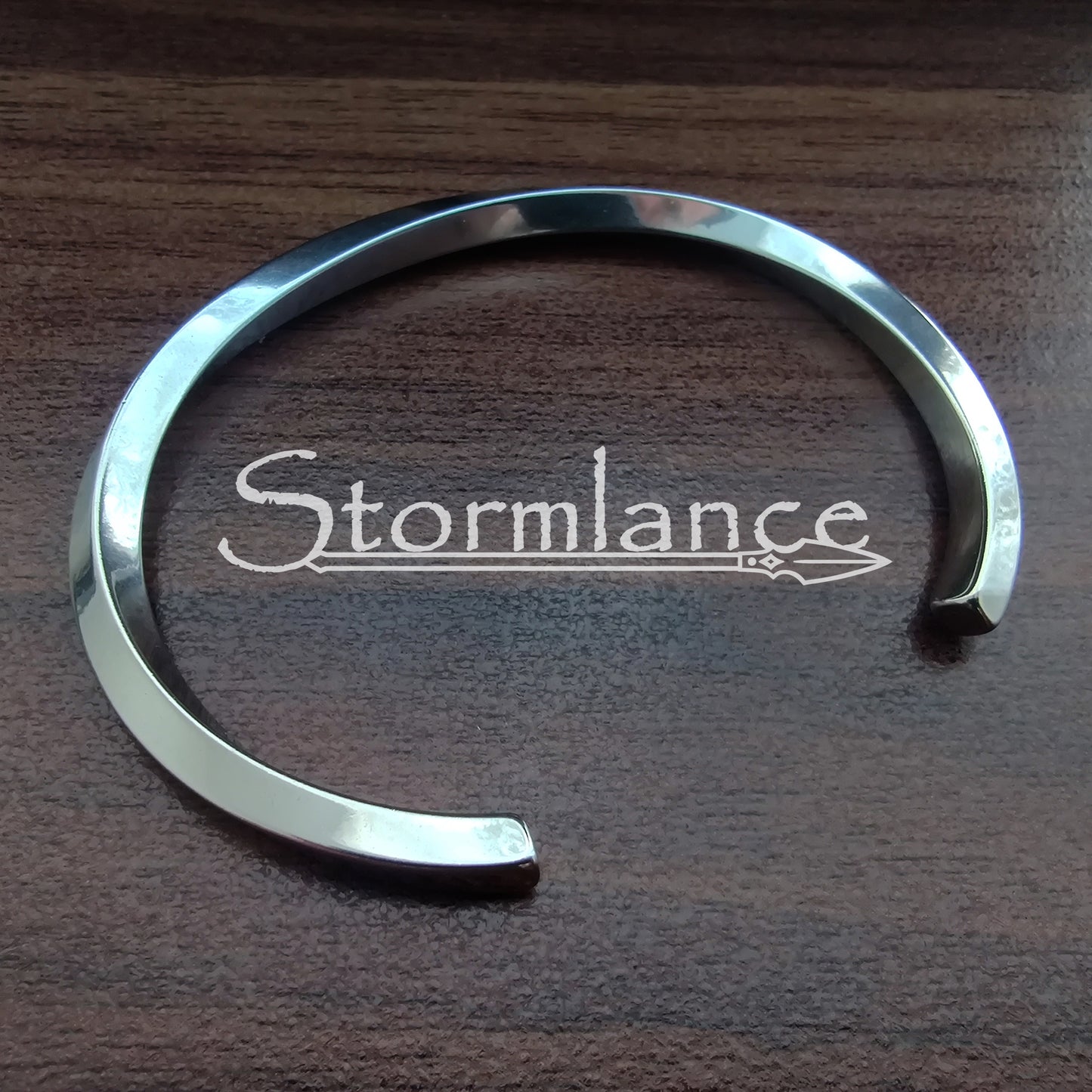 Shiny Twisted Simple Modern Arm Ring Made of Stainless Steel on a wooden background