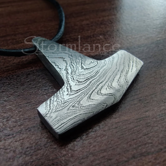 Small thor's hammer pendant, made of damascus steel, put on a wooden desk