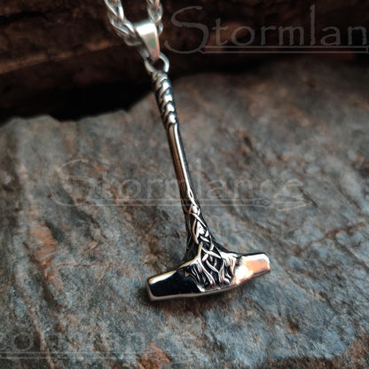 Small mjolnir pendant with long handle made of stainless steel, laying on a granite stone slab