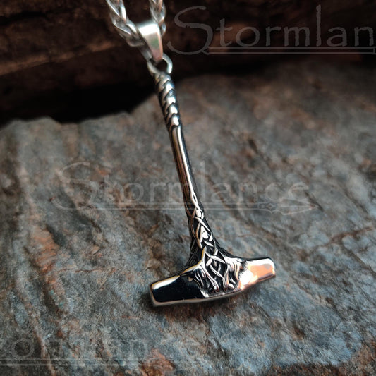 Small mjolnir pendant with long handle made of stainless steel, laying on a granite stone slab
