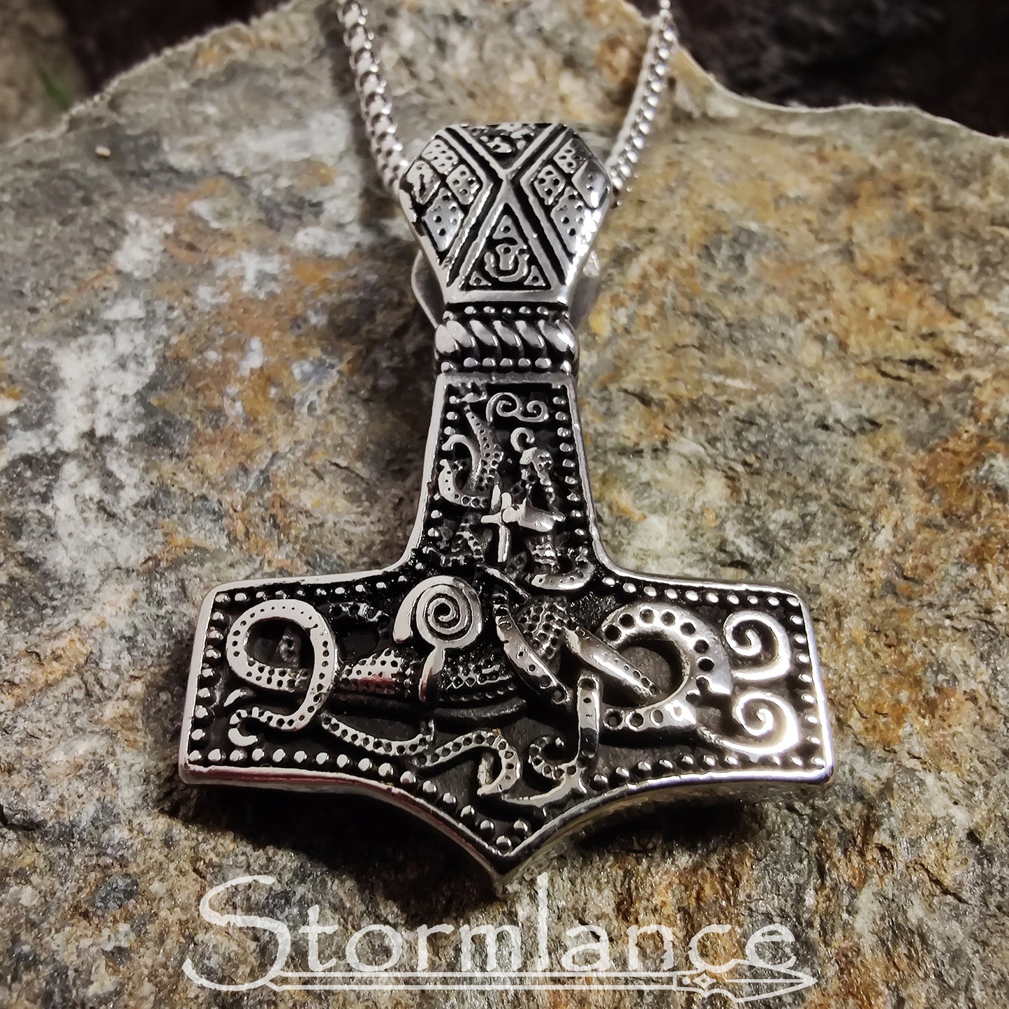 Scandinavian pattern Mjolnir pendant made of stainless steel, laying on a granite stone slab