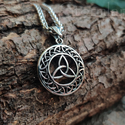 Triquetra pendant made of stainless steel, laying on a wooden slab