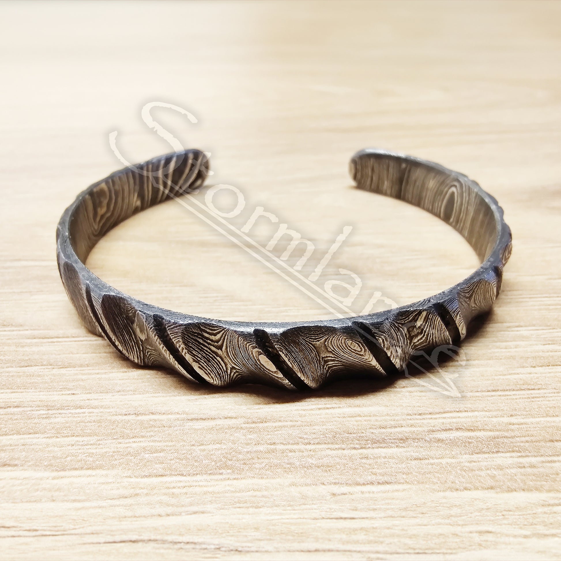 Twisted Cut Pattern Bracelet made of Damascus Steel laying on a wooden table