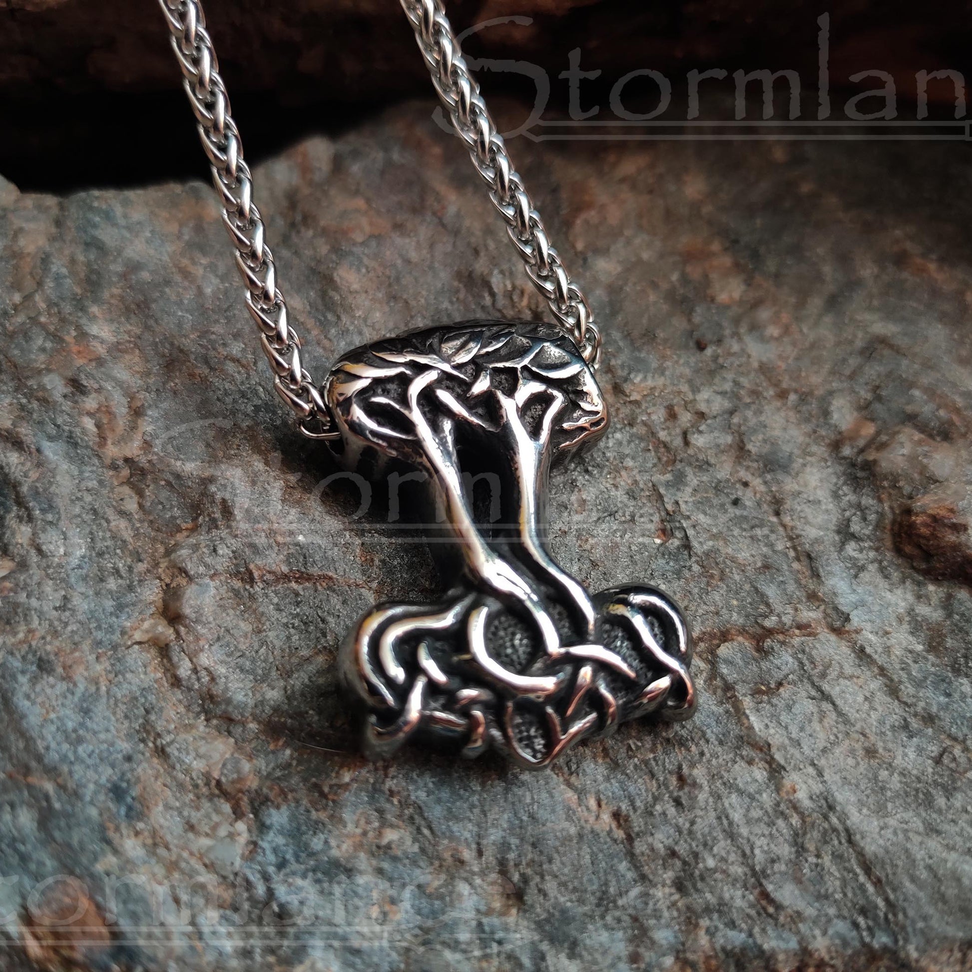 tree of life and thor's hammer in one pendant made of stainless steel, laying on a granite stone slab
