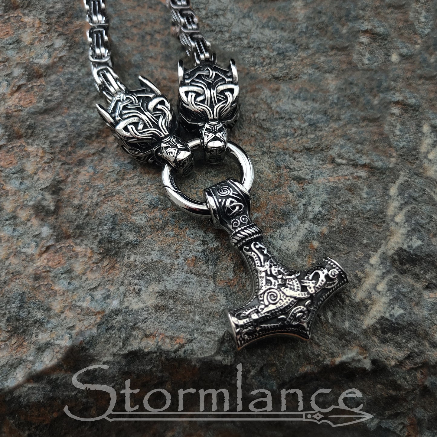 massive thor's hammer pendant with geri and freki wolves, made of stainless steel, laying on granite stone slab