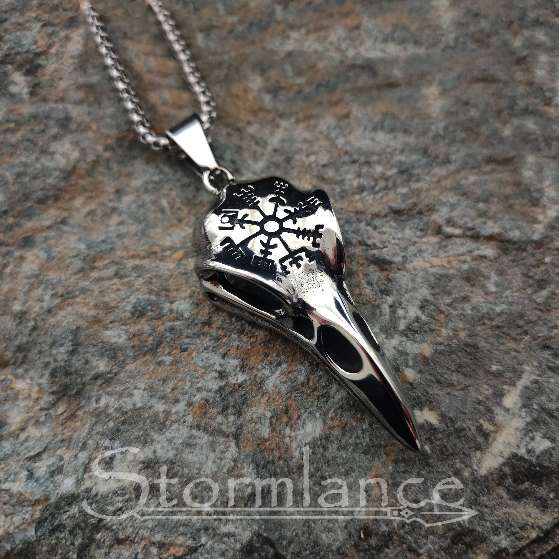 raven skull pendant with vegvisir made of stainless steel, laying on granite stone slab